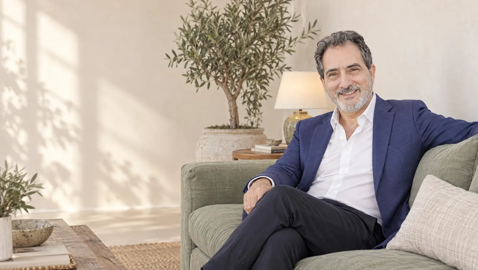 Steven Corn, mediator, smiling in a navy blazer on a sage sofa in a bright, spacious living room